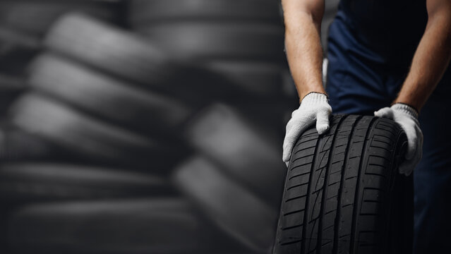 Portrait man mechanic holding new tyre on background store, car tire service concept