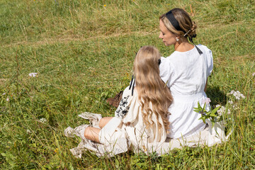 mother and daughter sitting on the grass in a green meadow on a warm summer day and talking