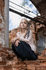 little girl 7 years old on the ruins of a building, the consequences of a disaster or war