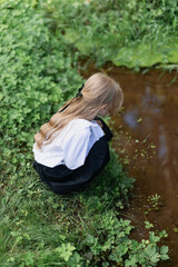 preschool girl stands on the bank of a stream and looks into the water