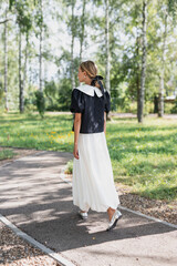 young girl in white blouse and black skirt walks in green park she smiles and is happy