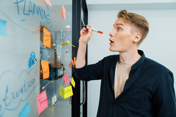 Professional caucasian male leader writing and sharing marketing idea by using mind map and sticky notes on glass board at modern meeting room. Creative business and planing concept. Immaculate.