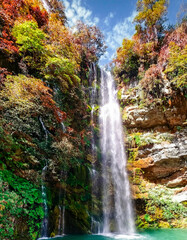Cascada de agua entre rocas y vegetaci&oacute;n de colores.