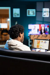 BIPOC person working in personal office, checking statistical data financial graphs on laptop screen. Freelancer in apartment living room comparing business graphic economic numbers