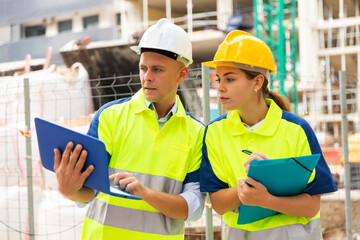 Two qualified engineers working on a construction site are discussing an important project, holding a laptop and an estimate ..in their hands