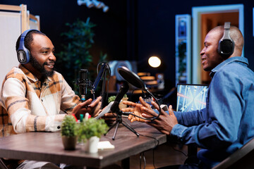 Serious talk between two black guys is being recorded for the online audience. Male African American content creators utilizing audio equipment while seated at home to make a podcast episode.