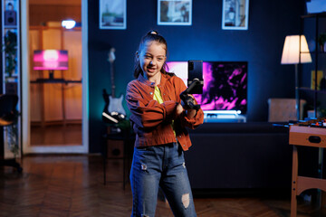 Cute kid holding smartphone attached to selfie stick, filming herself doing room tour for children...