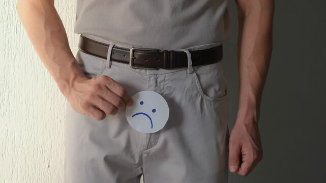Prostatitis and prostate cancer concept. Problems with erection and urination. A man shows a sad smiley face on paper near the zipper of his pants