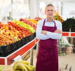 Portrait of confident salesman of fruit and vegetable store standing near counters..