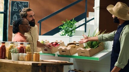 Vendor shows fresh produce to clients in local zero waste eco store, storekeeper recommending...