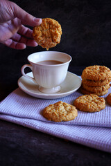 Traditional Australian Anzac Biscuits. Male hand dipping biscuit in cup of tea.