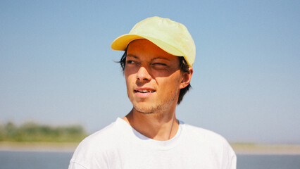 Portrait of a man in a yellow cap enjoying a sunny day outdoors, captured with a squint and a slight smile.