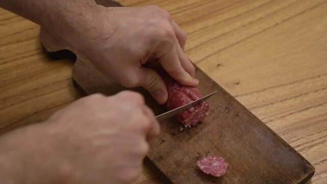 Antipasti. Top view of a man slicing a salami with a knife and a wooden cutting board