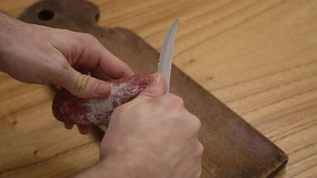 Antipasti. Closeup view of a man peeling a delicious salami with a knife 