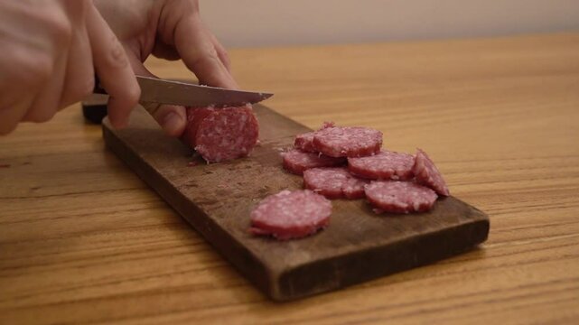 Antipasti. Closeup view of a man slicing a salami with a knife and a wooden cutting board