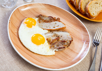 Healthy hearty lunch of sunny side up eggs accompanied by slices of fried bacon on rustic plate ..