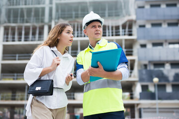 Builder in uniform and hardhat talking with woman about project documentation.