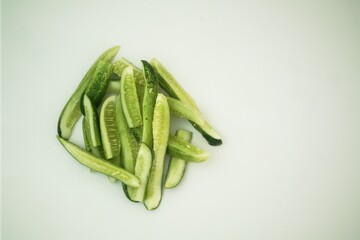 A pile of fresh, thinly sliced green vegetables, likely gourds or cucumbers, rests on a pristine white surface, offering clean copy space