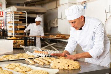 man in chefs uniform kneading dough in bakery