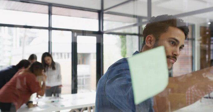 Business, man and writing on sticky note with smile in office for brainstorming, planning or reading. Employee, person and happy with problem solving, schedule or mind mapping on glass wall at work