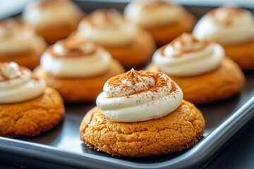 Freshly made pumpkin cookies, covered in a smooth cream cheese frosting and sprinkled with cinnamon, arranged on a baking sheet.






