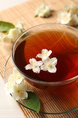 Hot jasmine tea in cup and flowers on white wooden table, closeup