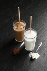 Delicious protein shakes in glasses and spoons with powder on black table