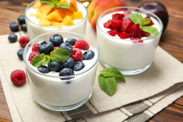 Tasty yogurt with fresh berries, fruits and mint in glasses on wooden table, closeup