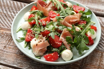 Tasty salad with arugula, mozzarella cheese, tomatoes and jamon on wooden table, closeup
