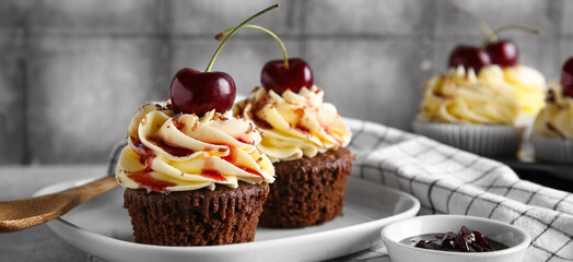 Plate with sweet cherry cupcakes and bowl of jam on grey table