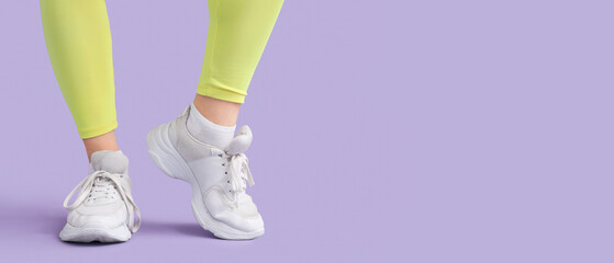 Female legs in white sneakers on lilac background with space for text