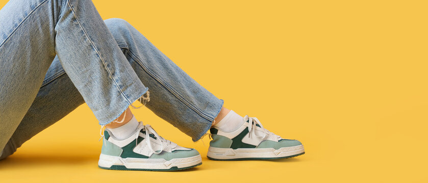 Female legs in stylish sneakers and jeans on yellow background with space for text