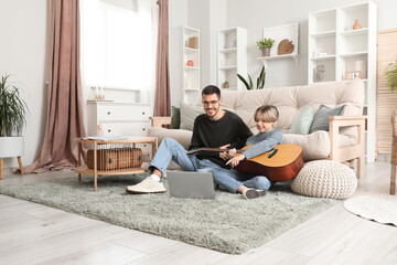 Private music teacher giving guitar lessons to little boy with online tutorial on laptop at home