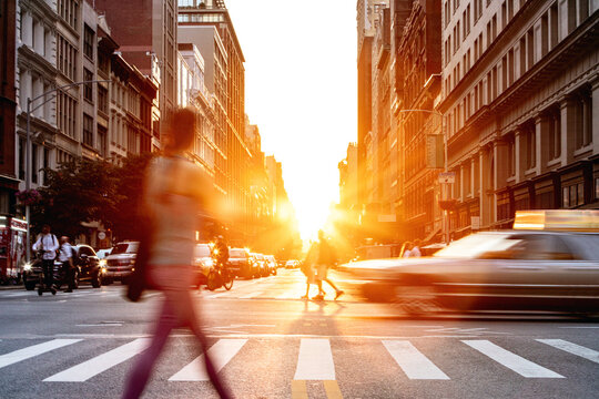 Person in motion walking through the busy intersection on 5th Avenue and 23rd Street in New York City with sunlight in background