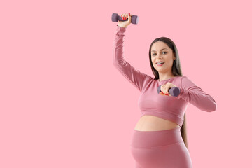 Sporty pregnant woman with dumbbells on pink background