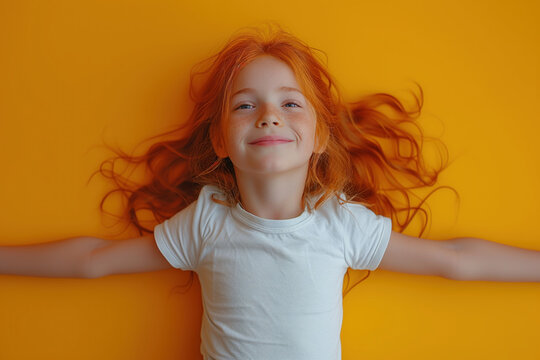 Happy redheaded child in white t-shirt laying on yellow background