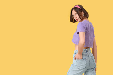 Beautiful young woman in stylish jeans on yellow background