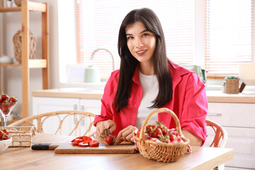 Beautiful young woman cutting fresh strawberries on table at home