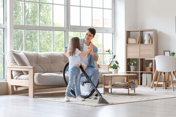 Young father and his daughter with vacuum cleaner giving high-five to each other at home