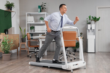 Young businessman running on treadmill in office