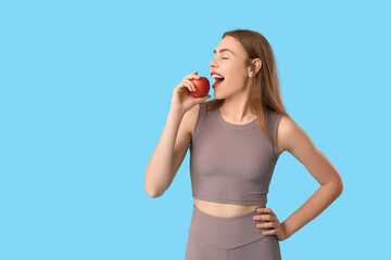 Sporty young woman eating apple on blue background. Diet concept