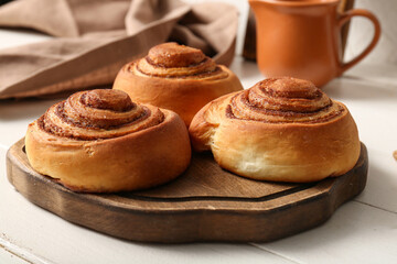 Board with sweet cinnamon rolls on white wooden table