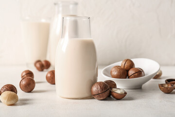 Bottle of fresh macadamia milk and bowl with nuts on white background