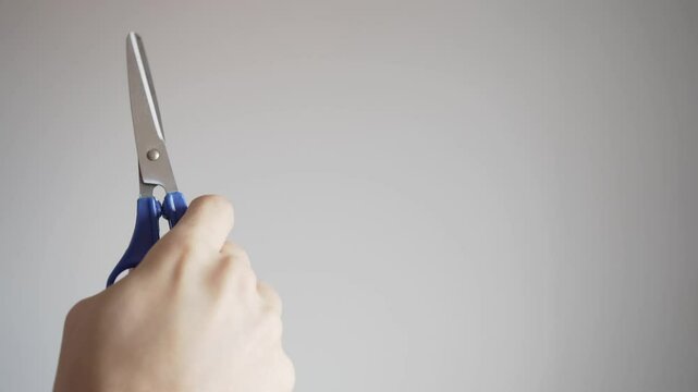 Blue scissors used on a neutral background. Hands using blue scissors with ample copy space on a grey background