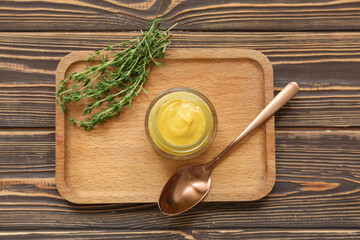 Board with jar of creamy mustard and spoon on brown wooden background