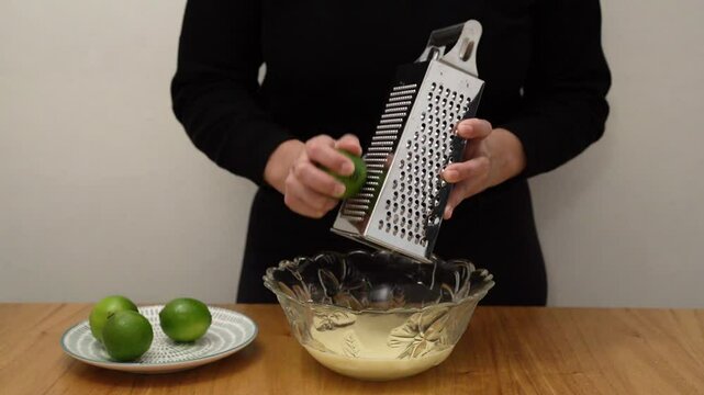 Bakery. Closeup view of a woman grating a lime with a metal rasper, into a bowl containing a citric cream.