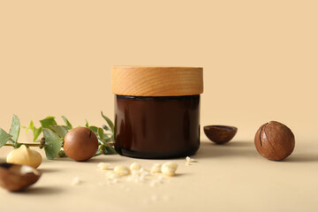 Macadamia nuts, green leaves and jar of cosmetic product on beige background, closeup