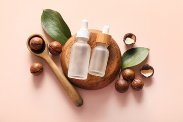 Macadamia nuts, spoon, wooden stand and bottles of cosmetic product on pink background