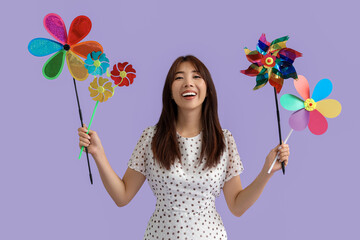Young Asian woman with toy windmills on lilac background