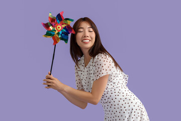 Young Asian woman with toy windmill on lilac background